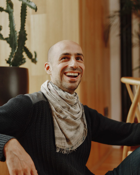 Man in cable sweater, with fringed scarf looking up and smiling.